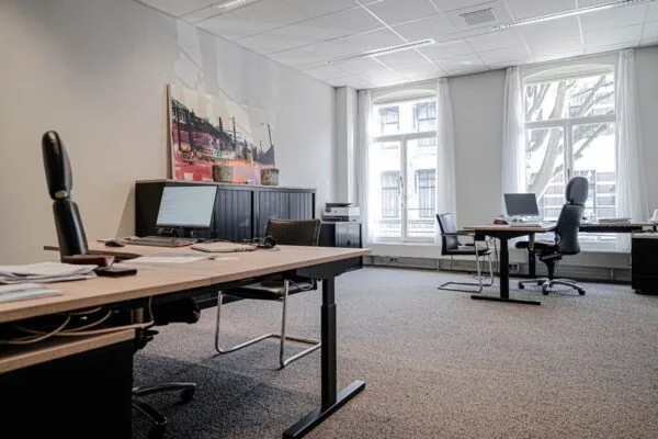 Modern kantoor aan de Burgemeester van Karnebeeklaan met meerdere bureaus, computers en grote ramen met uitzicht op de straat.